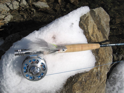 Rod and reel with white streamer on rock.